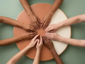 Diverse handen boven een ronde houten tafel die elkaar bijna raken, symbool voor samenwerking en consensus.