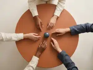 Diverse handen die samenkomen boven een ronde houten tafel, gefotografeerd van bovenaf in zachte natuurlijke belichting.