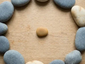 Kleine steen in het midden van een houten tafel, omringd door een losse kring van grotere stenen in ivoor- en leisteentinten.