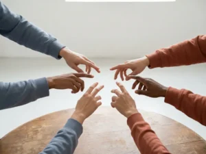 Diverse handen die samenkomen boven een ronde houten tafel, verlicht door zacht natuurlijk licht in warme terracotta en leisteenblauwe tinten.